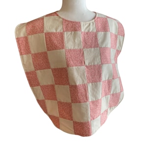 May include: A pink and white checkered baby bib with a floral pattern. The bib is made of quilted fabric and has a rounded neckline.