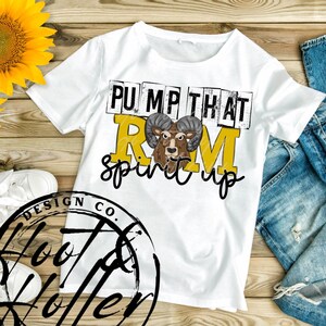 May include: White t-shirt with the text "PUMP THAT RAM spirit up" in black and yellow. The graphic features a ram's head. The shirt is on a wooden surface with a sunflower and a pair of jeans.