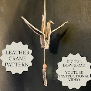 May include: A leather crane, with a tan and brown color scheme, is suspended by a string. The crane is made from folded leather. The image includes text that reads "Leather Crane Pattern" and "Digital Download + YouTube Instructional Video."