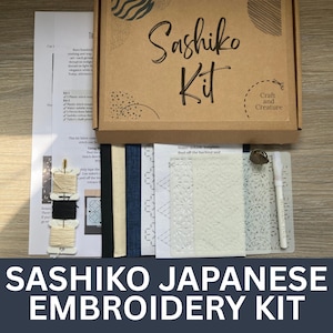 May include: A Sashiko Japanese embroidery kit in a brown box. The kit includes fabric, thread, a stencil, and a marking pen. The box has the words "Sashiko Kit" and "Craft and Creature" printed on it. The words "Sashiko Japanese Embroidery Kit" are printed at the bottom.