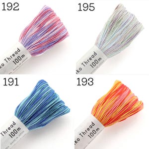 May include: Four skeins of variegated Sashiko thread, each labeled 100m and Made in Japan. The colors include pink and purple, light blue and white, shades of blue, and orange and yellow. Each bundle is secured with a white paper band.