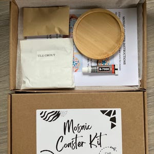 May include: A mosaic coaster kit in an open cardboard box. The kit includes a wooden coaster, tile grout, glue, and instructions. The box has a label that reads "Mosaic Coaster Kit".