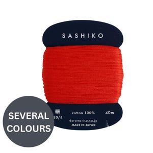 May include: A spool of bright red Sashiko thread wrapped around a dark blue cardboard card. The card features the text SASHIKO, cotton 100%, 40m, daruma-ito.co.jp, MADE IN JAPAN, and the Japanese characters for fine. A circular overlay says SEVERAL COLOURS.