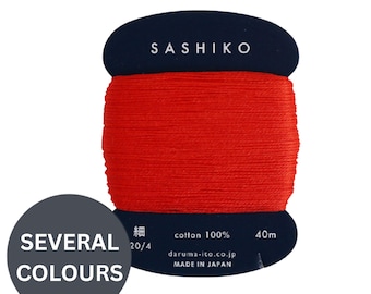 May include: A spool of bright red Sashiko thread wrapped around a dark blue cardboard card. The card features the text SASHIKO, cotton 100%, 40m, daruma-ito.co.jp, MADE IN JAPAN, and the Japanese characters for fine. A circular overlay says SEVERAL COLOURS.