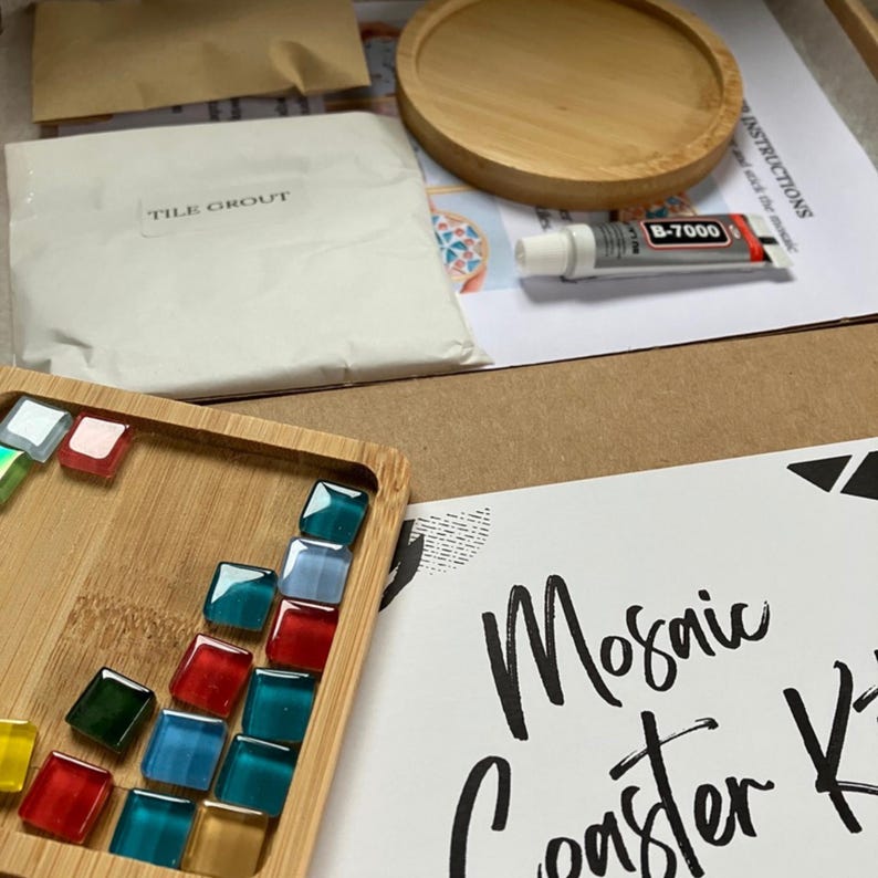 May include: A mosaic coaster kit with a wooden tray holding colorful glass tiles. The kit includes tile grout, a wooden coaster, and adhesive. The words "Mosaic Coaster Kit" are written on a white card.