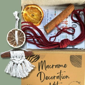 May include: A macrame decoration kit containing a dried orange slice, cinnamon stick, red cord, and a small macrame wall hanging. The kit includes instructions and is packaged in a cardboard box. The text "Macrame Decoration Kit" is visible.