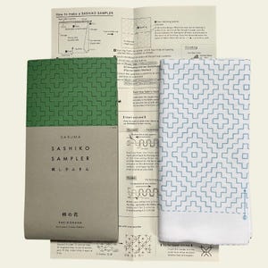 May include: A Sashiko sampler kit with instructions and a fabric piece. The kit includes a green and white booklet with Japanese text and a white fabric with a blue geometric pattern. The instructions are in English and Japanese.