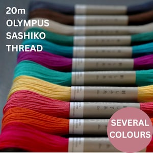 May include: A collection of Olympus Sashiko thread skeins, each 20m in length, arranged in a row. The threads feature a variety of vibrant colours including red, orange, yellow, teal, purple, blue, beige, brown, and black, with paper labels.