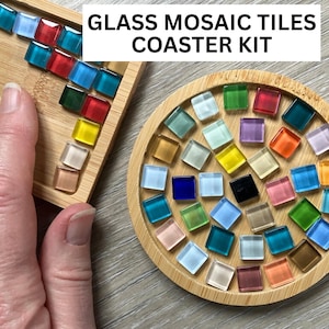 May include: A glass mosaic coaster kit with colourful square tiles in various colours, including red, blue, green, and yellow. The tiles are arranged on a wooden tray and a round wooden coaster. The text "GLASS MOSAIC TILES COASTER KIT" is at the top.