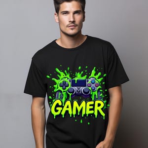 May include: Black t-shirt with a neon green graphic of a video game controller and the word "GAMER". The controller design has blue and purple accents, with a green splatter effect around it.