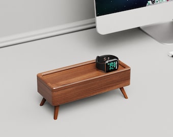 May include: A wooden watch stand with a watch on top. The stand has a rectangular base with rounded edges and four legs. The watch is black with a digital display showing the time 7:29.