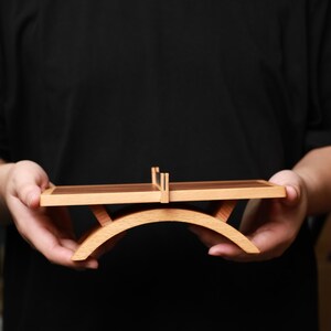 May include: A small, wooden table with a curved base and a rectangular top. The top is divided into two sections, one light-colored and one dark-colored. The table is held in front of a dark background.