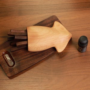 Op de afbeelding: Een houten pijl-vormige container met donkerbruine stokken erin, rustend op een donkerbruine houten snijplank. Een kleine zwarte fles met een etiket staat naast de container. De items staan op een houten oppervlak.