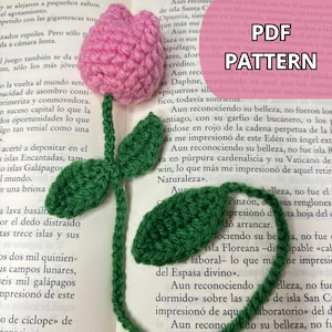 Può includere: Segnalibro all'uncinetto fatto a mano a forma di tulipano rosa con foglie e stelo verdi. Il segnalibro è posto su un libro aperto. Il testo "PDF PATTERN" è visibile.