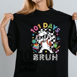 K&ouml;nnte beinhalten: Schwarzes T-Shirt mit einem Dalmatiner, der eine Sonnenbrille und einen Rucksack tr&auml;gt und dabbt. Das Shirt hat den Text "101 Days Bruh" und schulische Grafiken, einschlie&szlig;lich B&uuml;cher, Bleistifte und einen Globus.