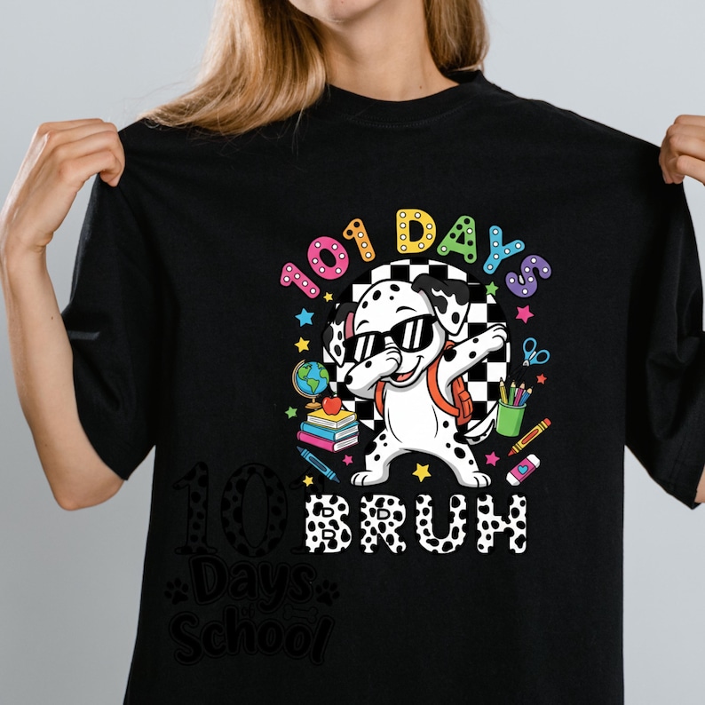 K&ouml;nnte beinhalten: Schwarzes T-Shirt mit einem Dalmatiner, der eine Sonnenbrille und einen Rucksack tr&auml;gt und dabbt. Das Shirt hat den Text "101 Days Bruh" und schulische Grafiken, einschlie&szlig;lich B&uuml;cher, Bleistifte und einen Globus.