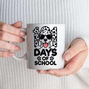 K&ouml;nnte beinhalten: Wei&szlig;e Keramik-Tasse mit einem Dalmatiner, der eine Sonnenbrille tr&auml;gt, und dem Text "101 DAYS OF SCHOOL" in Schwarz. Der Hund hat schwarze Flecken und eine rosa Zunge. Pfotenabdr&uuml;cke sind darunter.