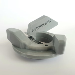 Puede incluir: Una pieza de plástico gris impresa en 3D con una palanca y una abertura circular. La pieza tiene la palabra "PROWORK" impresa en ella.