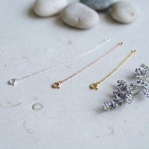 May include: Three delicate metal chain extenders featuring a circular spring ring clasp at one end. The set includes one silver-toned chain, one rose gold-toned chain, and one gold-toned chain, each with a fine link design for jewelry adjustment.