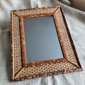 May include: A rectangular mirror with a woven bamboo frame. The frame is brown with a light brown woven pattern. The mirror is reflecting a blurry image.