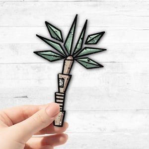 Könnte beinhalten: Ein grüner und brauner geometrischer Palmenbaum-Aufkleber. Der Palmenbaum hat einen segmentierten Stamm und eine stilisierte Blätterkrone.