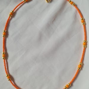May include: A simple orange and gold beaded necklace with a gold clasp.