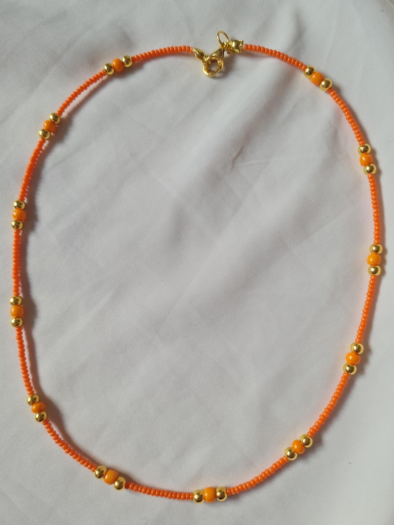 May include: A simple orange and gold beaded necklace with a gold clasp.