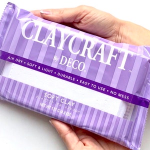 Könnte beinhalten: Eine violette und weiße Packung mit weicher Claycraft-Modelliermasse von Deco. Die Verpackung trägt den Schriftzug "Air Dry, Soft & Light, Durable, Easy to Use, No Mess". Außerdem steht auf der Verpackung "Soft Clay" und "クレイクラフト デコ ソフトクレイ" in japanischer Sprache. Die Verpackung trägt den Schriftzug "Net Wt 137 g (4.8 oz)".