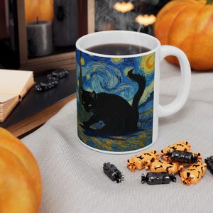Könnte beinhalten: Weiße Keramiktasse mit einer schwarzen Katzenillustration vor einem wirbelnden blau-gelben Sternenhintergrund. Die Tasse ist mit dunkler Flüssigkeit gefüllt und von Halloween-Süßigkeiten umgeben.