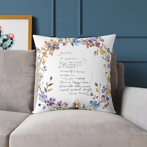 Könnte beinhalten: Quadratisches weißes Kissen mit einem floralen Kranz in Blau, Lila, Gelb und Orange. Das Kissen hat handgeschriebenen Text, der lautet: "Liebe Kind, Worte können nicht sagen, wie sehr ich dich liebe, dich als Tochter zu haben..." und ist mit "Love Mom" signiert.