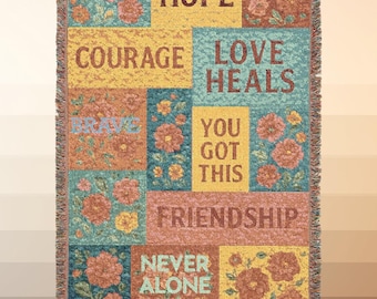 May include: Woven throw blanket with a patchwork design. The blanket features floral patterns and inspirational words like "Hope," "Courage," and "Friendship." The color palette includes shades of yellow, teal, and coral, with a fringed edge.