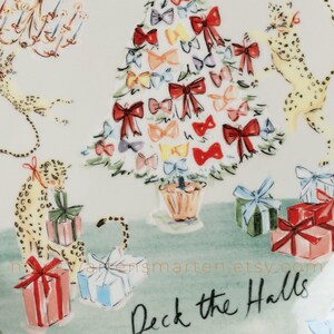 May include: A decorative plate with a festive Christmas theme. The design features a Christmas tree adorned with colorful bows, playful leopards, and wrapped gifts. The phrase "Deck the Halls" is written in black script.