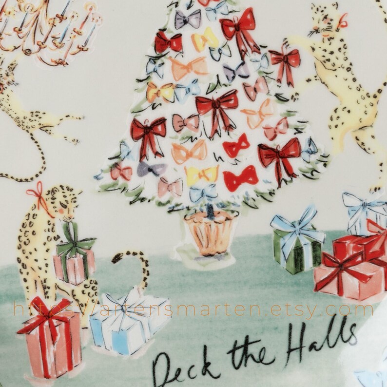 May include: A decorative plate with a festive Christmas theme. The design features a Christmas tree adorned with colorful bows, playful leopards, and wrapped gifts. The phrase "Deck the Halls" is written in black script.