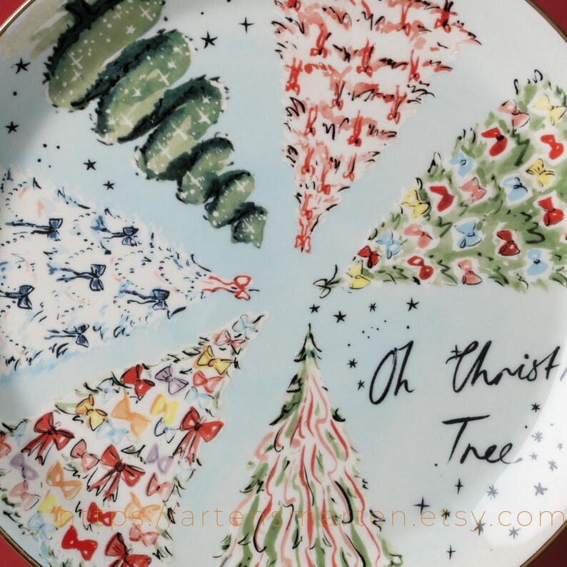 May include: A decorative plate with a light blue background featuring stylized Christmas trees in various colors and patterns. The plate has a gold rim and the words "Oh Christmas Tree" are written in black script.