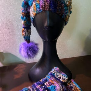 May include: A handmade crochet hat and matching fingerless gloves set. The hat is a mix of blue, purple, orange, and brown yarns, with a long, pointed end and a purple pom-pom. The gloves have a similar color scheme.