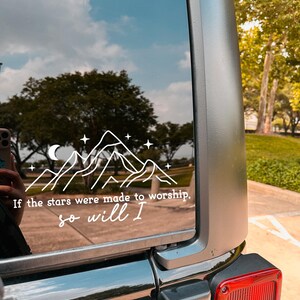 May include: A black car with a white vinyl sticker on the back window. The sticker features a mountain range with a crescent moon and stars. The text on the sticker reads "If the stars were made to worship, so will I."