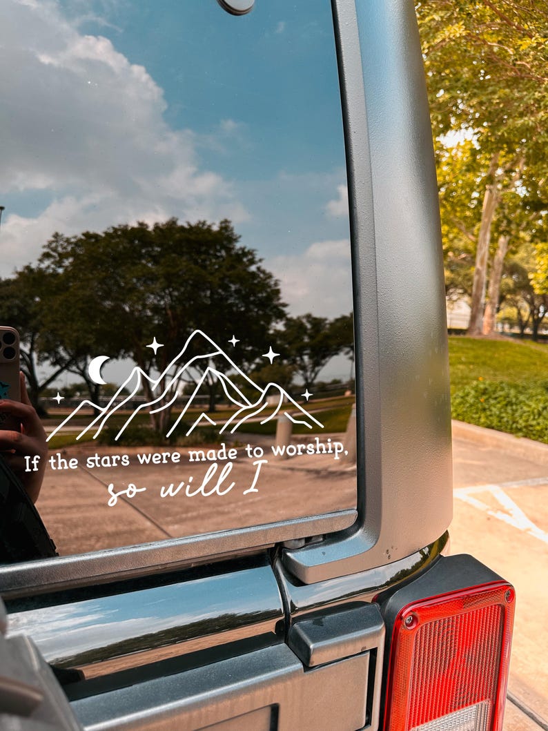 May include: A black car with a white vinyl sticker on the back window. The sticker features a mountain range with a crescent moon and stars. The text on the sticker reads "If the stars were made to worship, so will I."