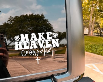 May include: White vinyl decal applied to a vehicle window. The decal reads "MAKE HEAVEN crowded" in a stylized font, with a cross symbol at the bottom. The background shows a sky with clouds and trees.