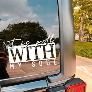 May include: A black car with a white vinyl decal on the back window that reads "it is well WITH MY SOUL".