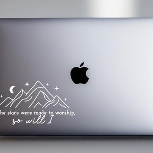 May include: A silver laptop with a white sticker featuring a mountain range, a crescent moon, and stars. The sticker also includes the text "If the stars were made to worship, so will I."