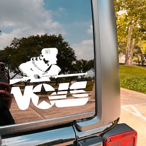 May include: A white vinyl decal of a soldier holding a rifle with the word "VOLS" and a star underneath. The decal is on the back window of a black car.