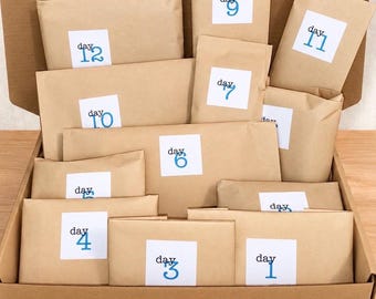 May include: A cardboard box filled with multiple brown paper packages of varying sizes. Each package features a white square label with the word day followed by a blue number, ranging from one to twelve, indicating a countdown or advent calendar set.