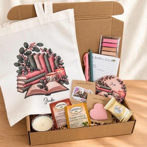Può includere: Una scatola regalo contenente una borsa di tela bianca con un'illustrazione di libri e fiori, un'etichetta rosa a forma di cuore, due bustine di tè Twinings, una candela, una penna, un blocco note, foglietti adesivi, un sottobicchiere rotondo e un cioccolatino Ferrero Rocher.