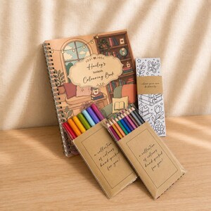 Puede incluir: Un libro de colorear de espiral titulado Hailey's bookish Colouring Book, un marcap&aacute;ginas vertical con arte lineal de flores y mariposas, y dos juegos de l&aacute;pices de colores en fundas de papel marr&oacute;n con la etiqueta a collection of colours hand-picked for you.