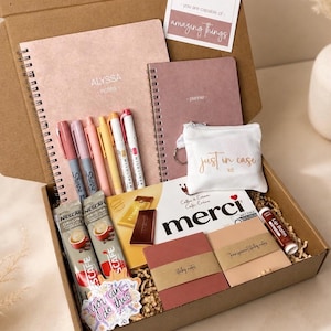 May include: A gift box containing stationery and treats. It includes a spiral notebook, pens, sticky notes, coffee sachets, chocolate bars, and a small pouch. The box also has a card with the text "you are capable of amazing things."