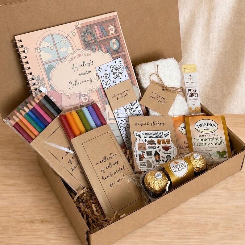 Puede incluir: Una caja de regalo que contiene un libro para colorear de espiral etiquetado Hailey's bookish Colouring Book, l&aacute;pices de colores, un marcap&aacute;ginas, calcetines blancos esponjosos con una etiqueta a hug for your feet, miel, pegatinas y bombones Ferrero Rocher.