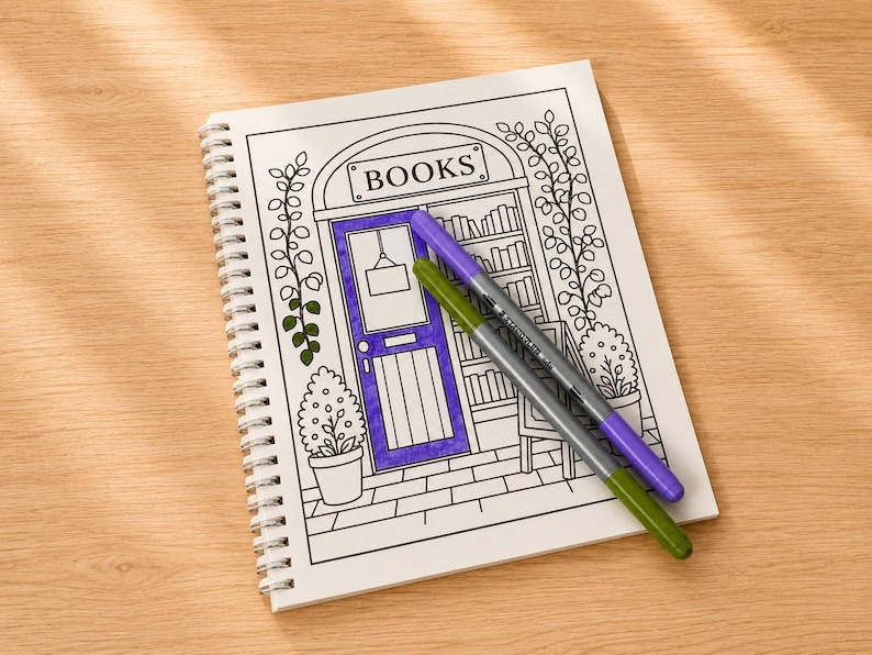 Puede incluir: Una p&aacute;gina de libro para colorear con espiral que presenta una ilustraci&oacute;n de l&iacute;neas de la fachada de una librer&iacute;a con la palabra BOOKS impresa sobre la puerta. La puerta est&aacute; coloreada en morado y dos rotuladores, uno morado y otro verde, descansan.