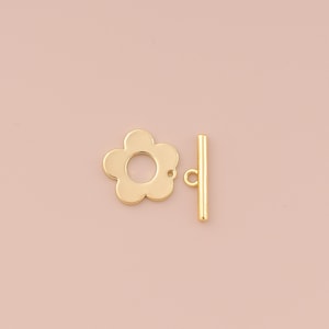 Op de afbeelding: Gouden metalen bloemenvormige toggle sluiting met een rechte staaf. De sluiting is een populaire keuze voor kettingen, armbanden en andere sieradenprojecten.