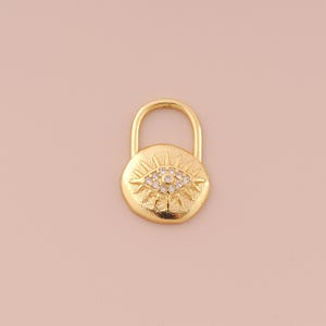 May include: Gold charm with a detailed evil eye design with clear rhinestones. The charm is shaped like a padlock.