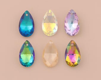 May include: Six iridescent teardrop-shaped crystal beads in shades of blue, yellow, purple, and green. Each bead has a faceted surface and a small hole at the top for stringing. The beads are arranged on a light pink background.